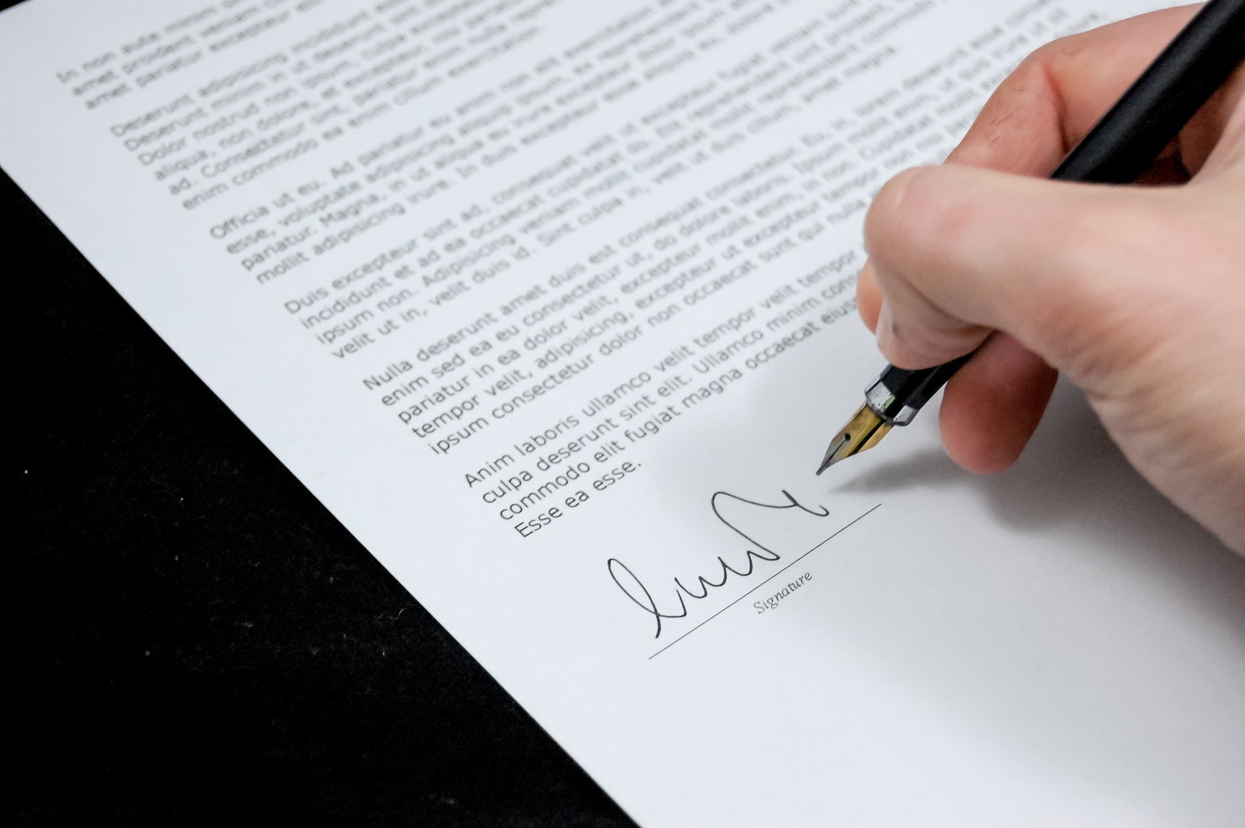 Una persona firma un documento con una pluma. El documento hace referencia a una licencia.